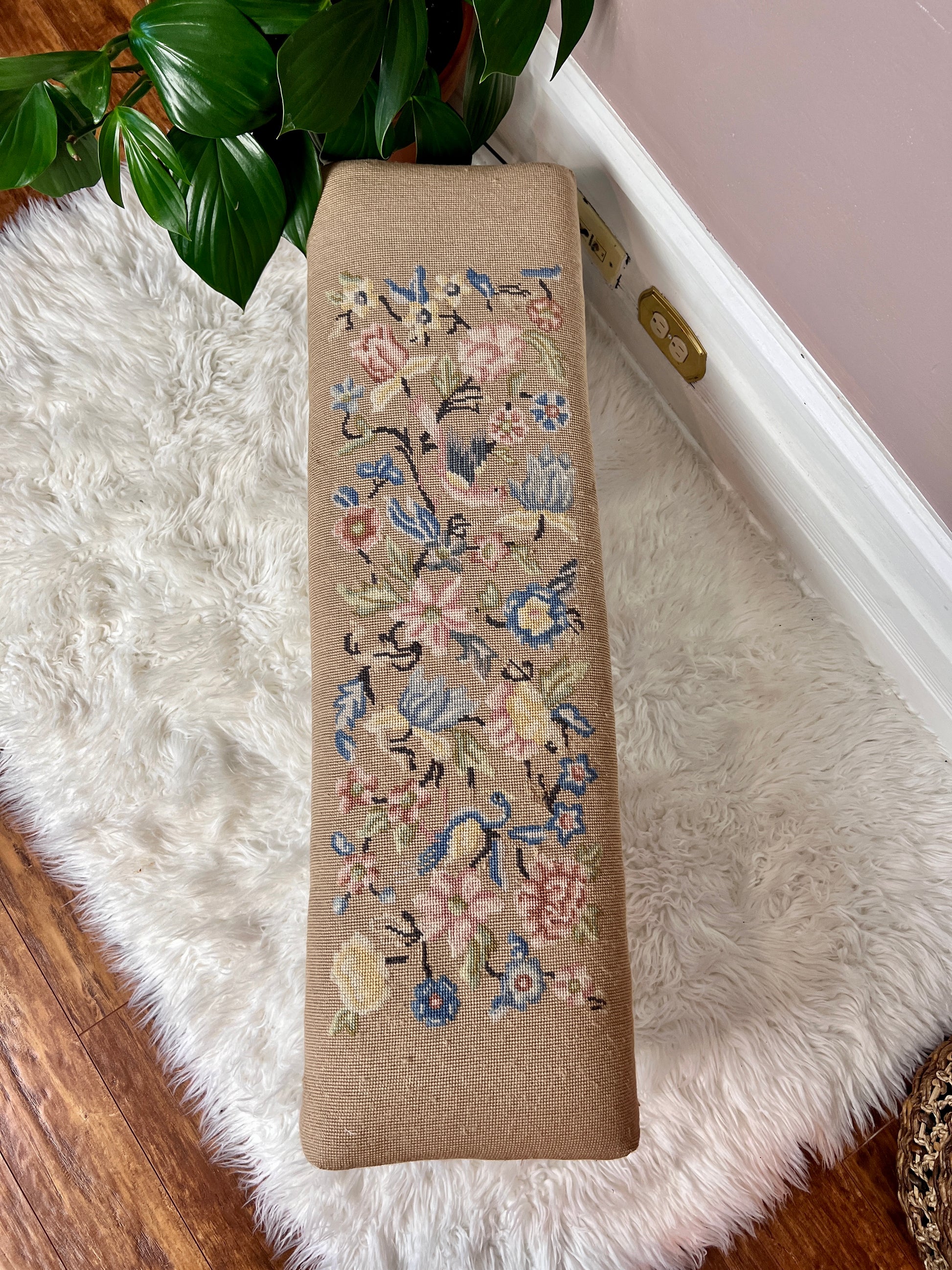 This is a antique beige ottoman footstool with pink and blue floral patterns with birds as well.