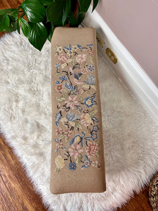 This is a antique beige ottoman footstool with pink and blue floral patterns with birds as well.