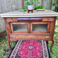 This is a unique antique wooden hutch with a cream colored tiled top that could used as a kitchen island